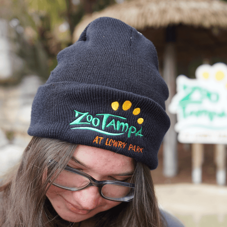 Girl with glasses and brown hair looking down while wearing a black ZooTampa logo beanie.