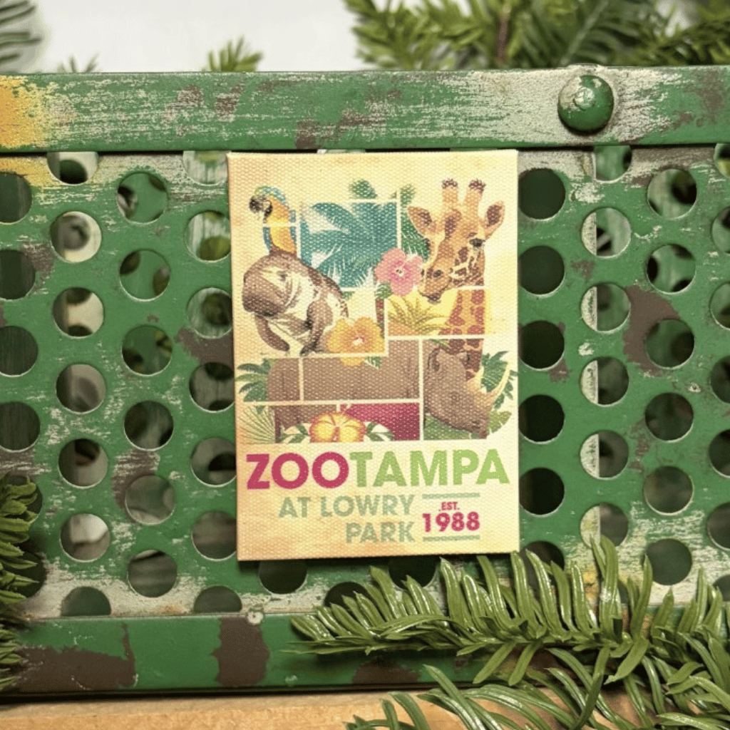 A vintage-style ZooTampa at Lowry Park 1988 canvas style magnet distressed green metal crate with pine branches in the background.