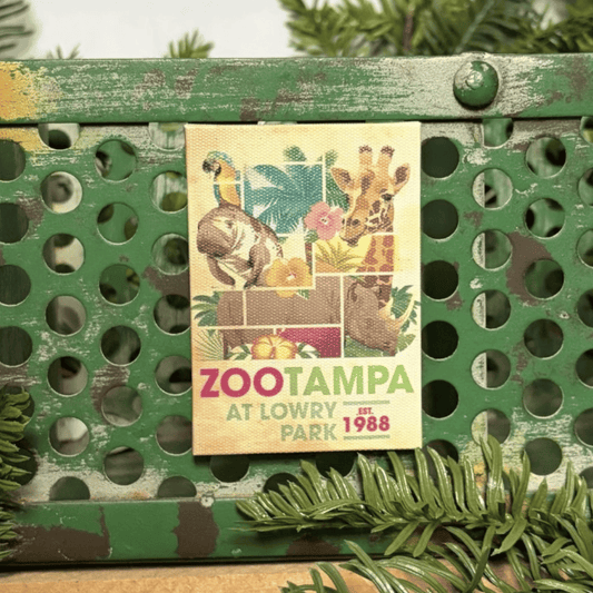 A vintage-style ZooTampa at Lowry Park 1988 canvas style magnet distressed green metal crate with pine branches in the background.