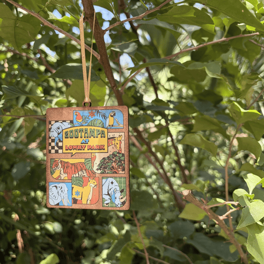 ZooTampa Ornaments hanging from a tree branch. The ornaments features a giraffe, tiger, elephant, rhino, and more in a comic style design.